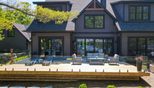 The back of a large, modern cottage with two stories and many wide windows. A large deck with a glass railing branches off the house.