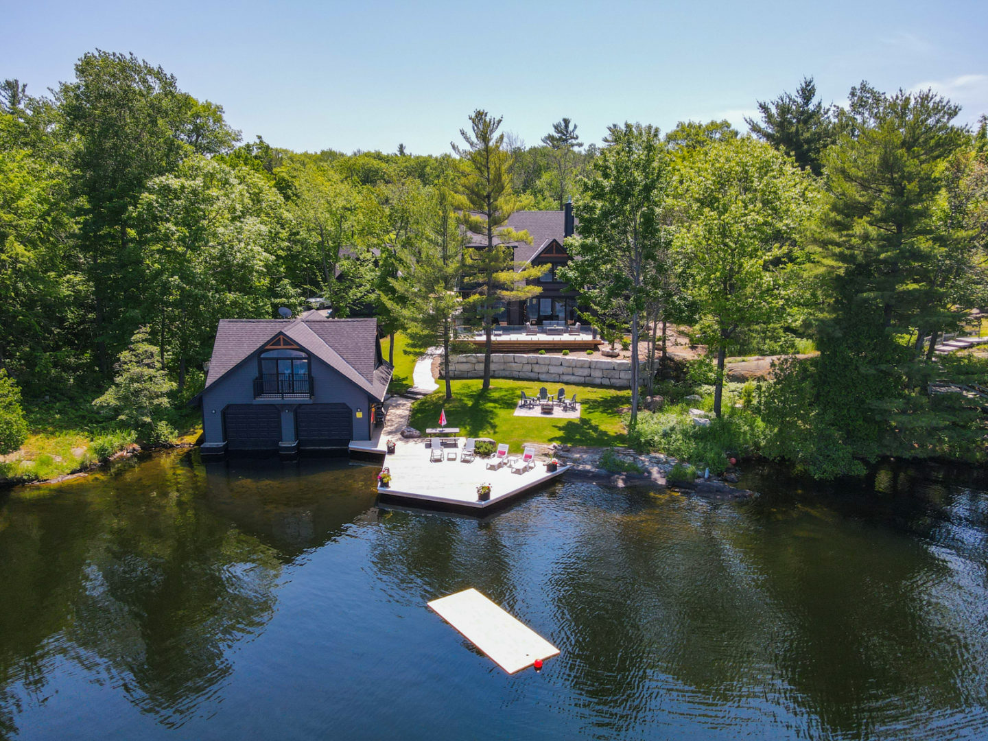 A large lakefront property with a boathouse and a big dock on the water, and a large cottage surrounded by trees.