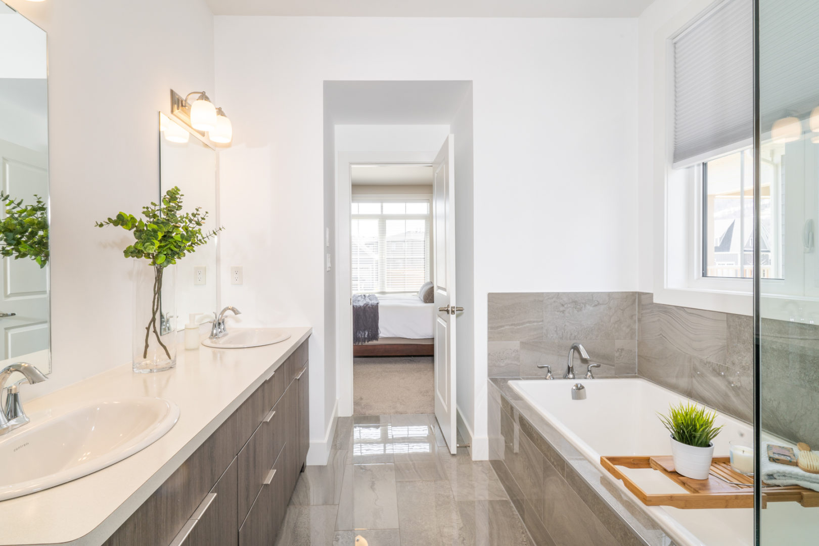 A large bathroom with double sinks and a bathtub, looking out into a large bedroom.