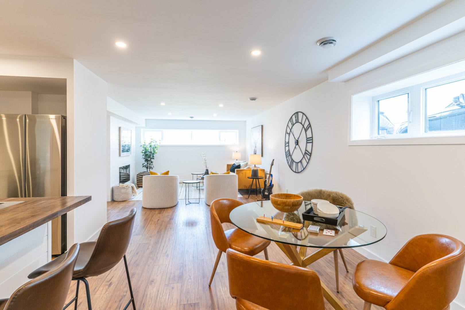 A bright, open-concept basement living area with a table and chairs and a living room area in the background.