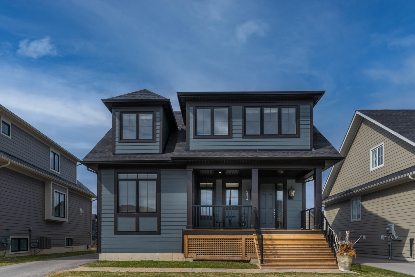Front exterior of a newly built two-story home with dark blue siding, large windows, and a big front porch.