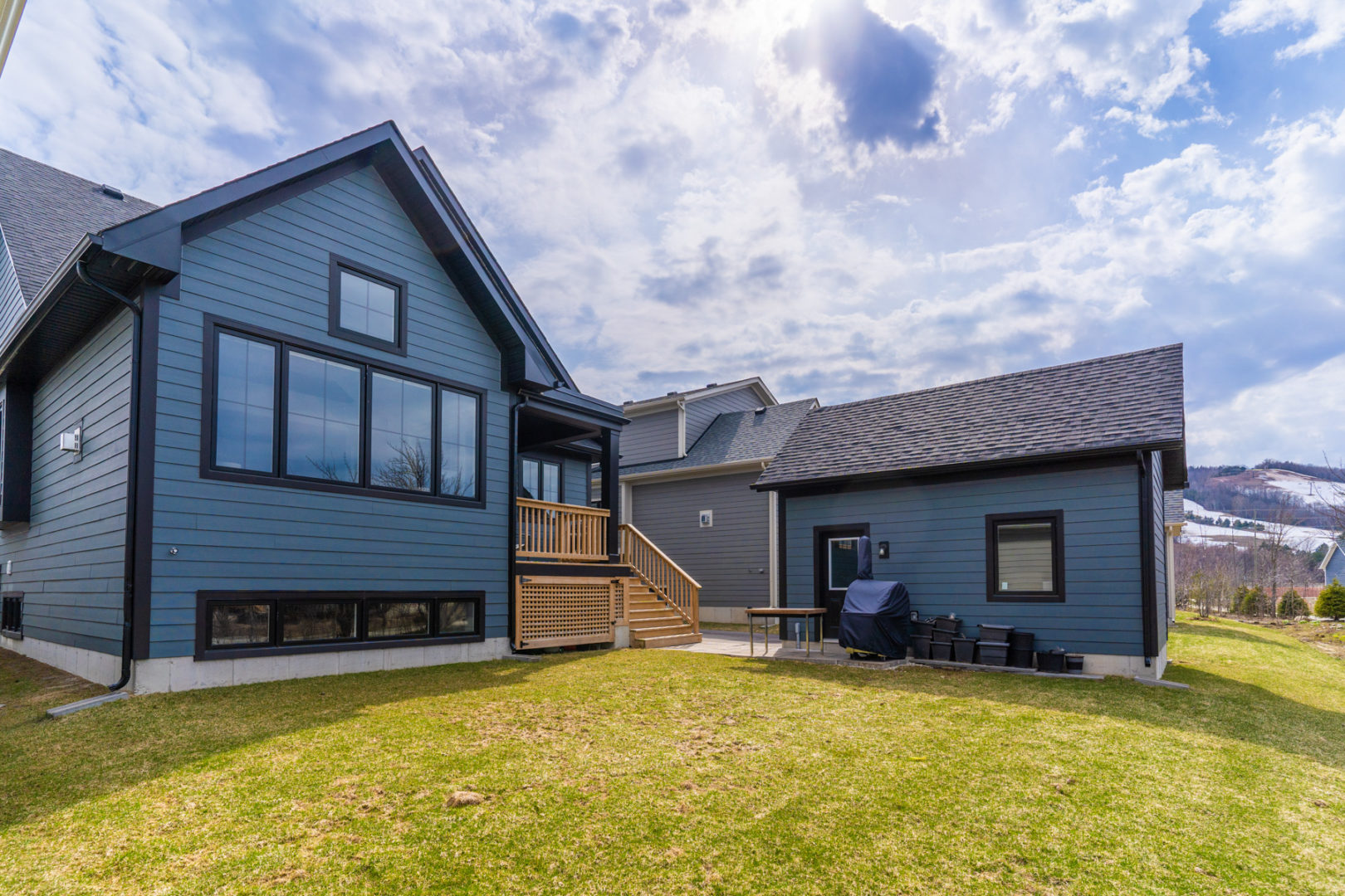 A spacious, grassy backyard of a two-story house with a dark blue exterior, a small back deck, and a detached single car garage.