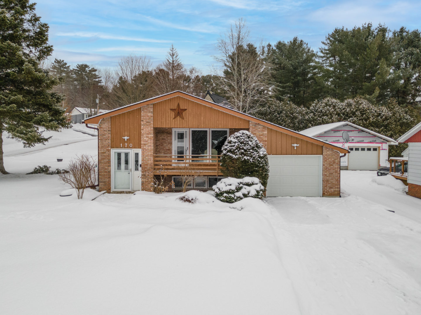 The front of a house with a single car garage and a front balcony, in a small neighborhood surrounded by trees.