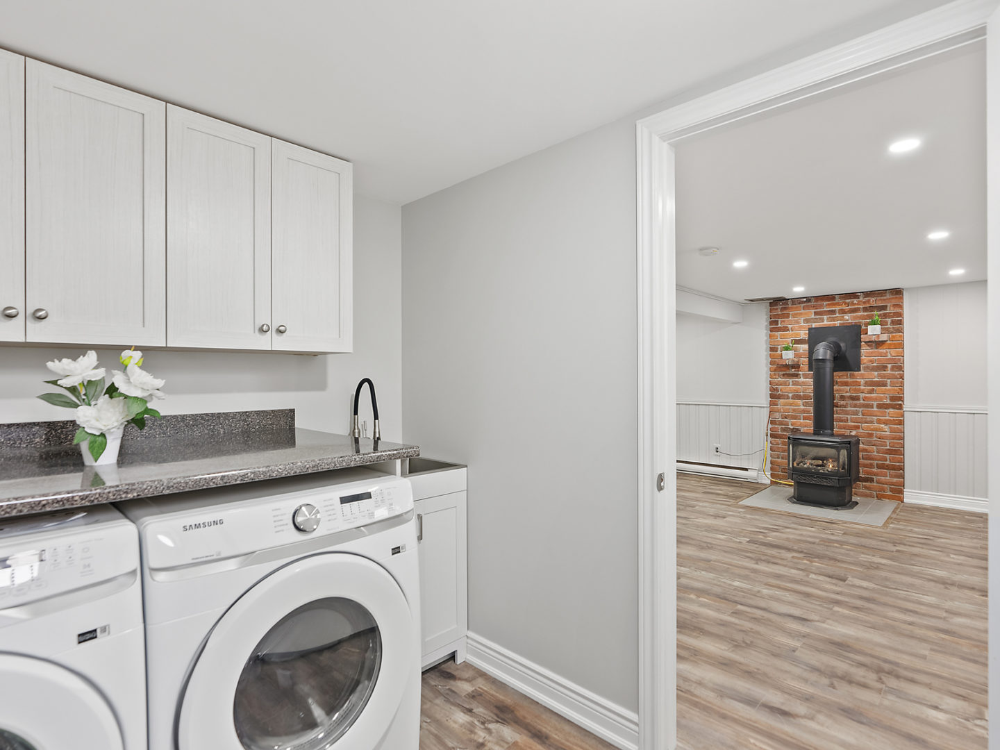 A space with a washing machine and dryer, leading into a larger room with hardwood floors and a fireplace. Bright and newly renovated.