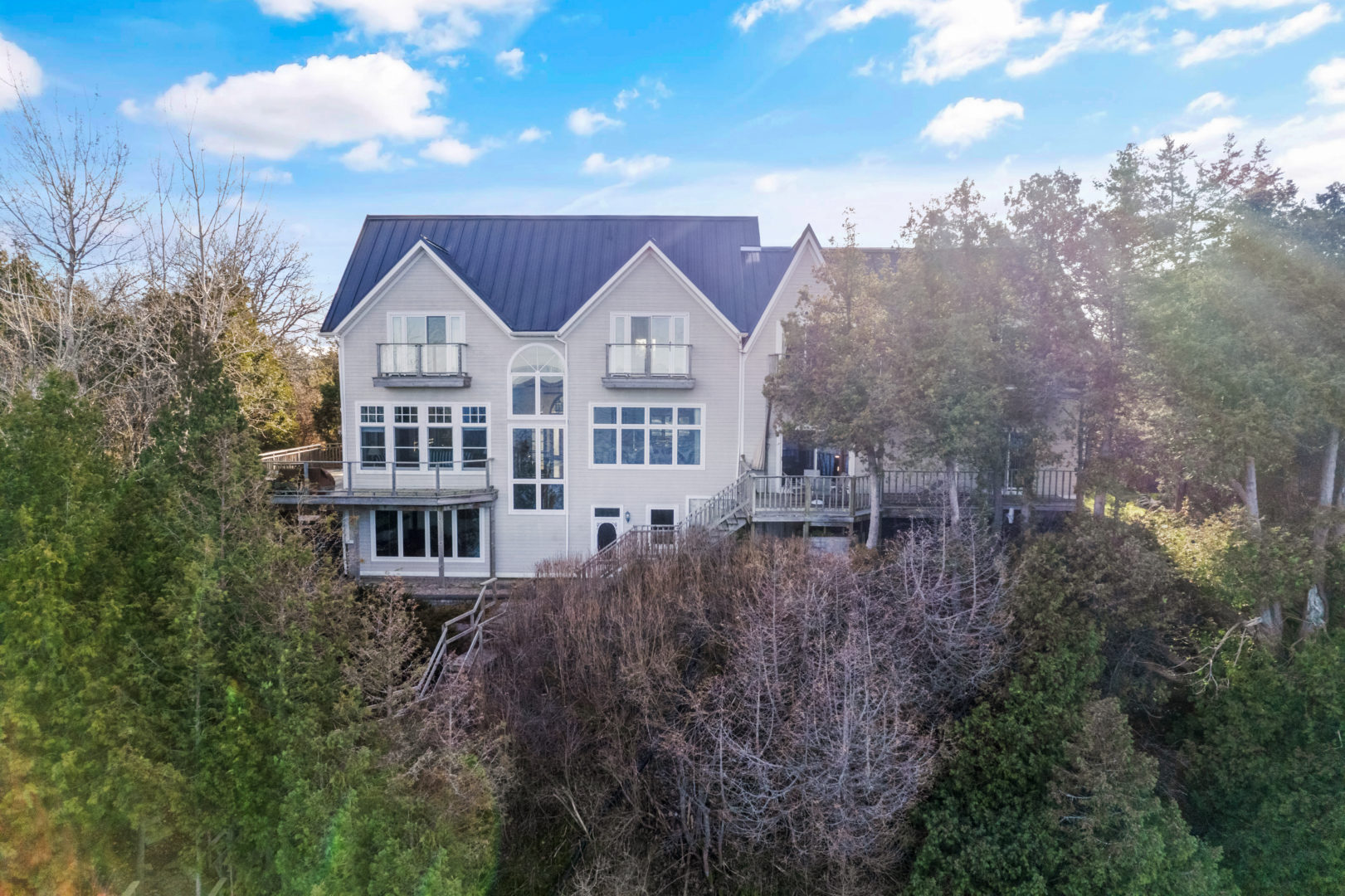 Waterfront view of a large lake house with lots of windows and balconies looking out toward the water.