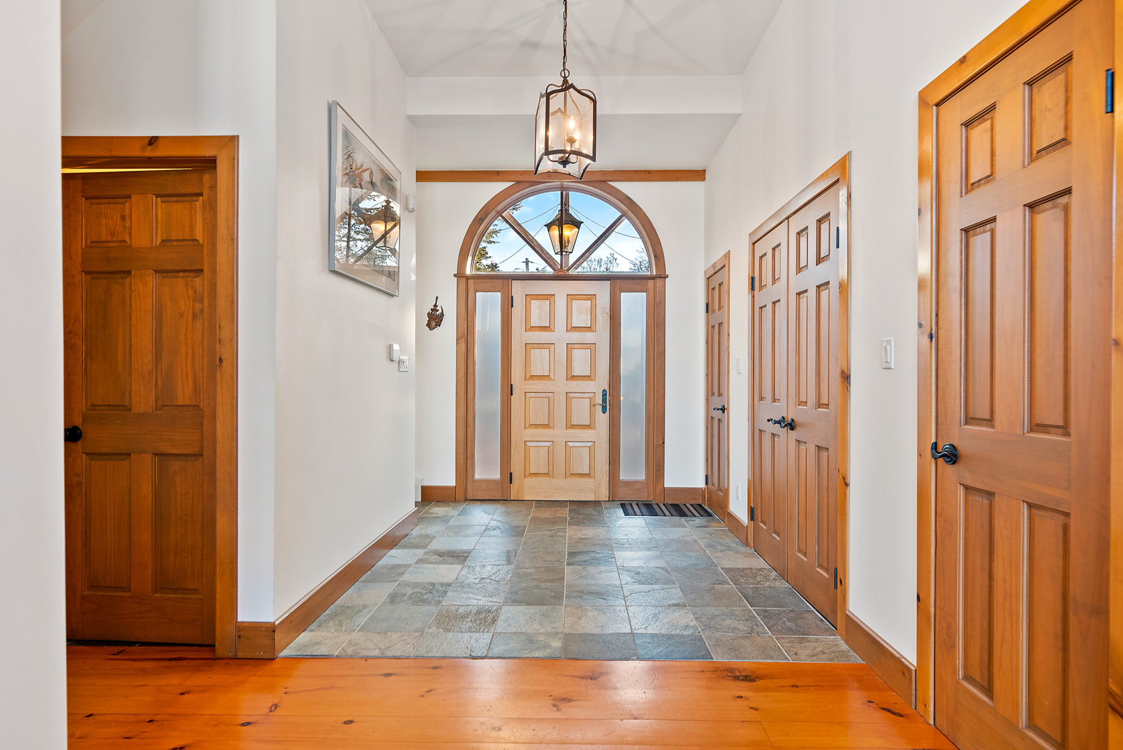 A large, bright entrance area of a house. A big stretch of tile extends throughout the space in front of the door, and then transitions into light-coloured hardwood floor.