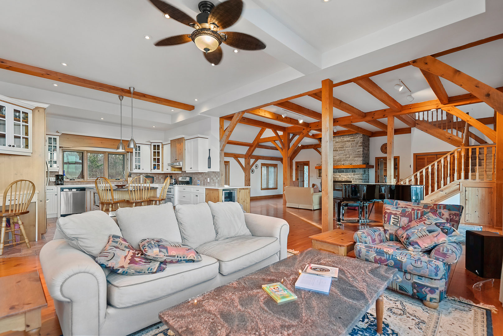 A couch and chairs offer a small sitting area as part of a broader open-concept space. A small kitchen and a grand piano lay beyond the couch.