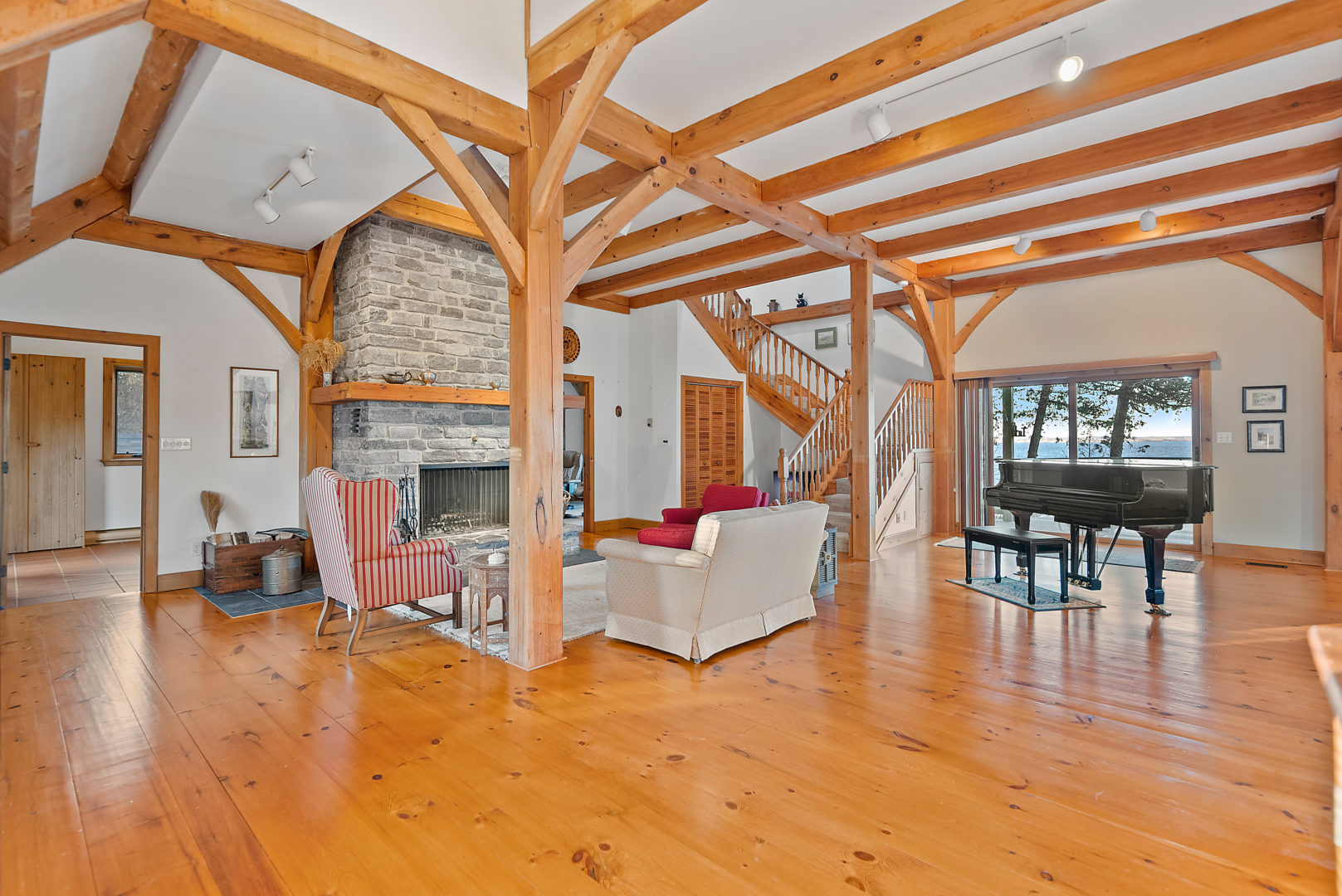 A bright, spacious living area with a couch and chairs sitting around a stone fireplace. A grand piano sits in front of a large window.