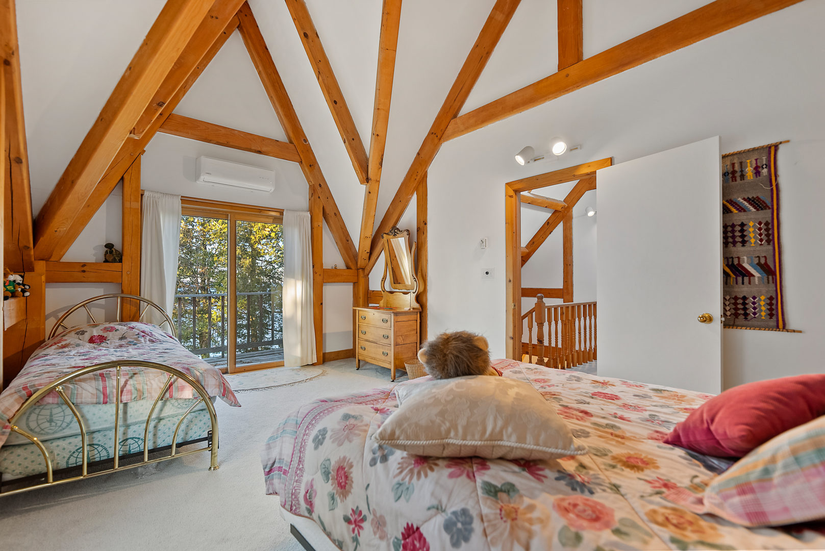 A small, bright bedroom with two single beds. Slanted walls, painted white with wooden beam accents, come to a point in the ceiling.