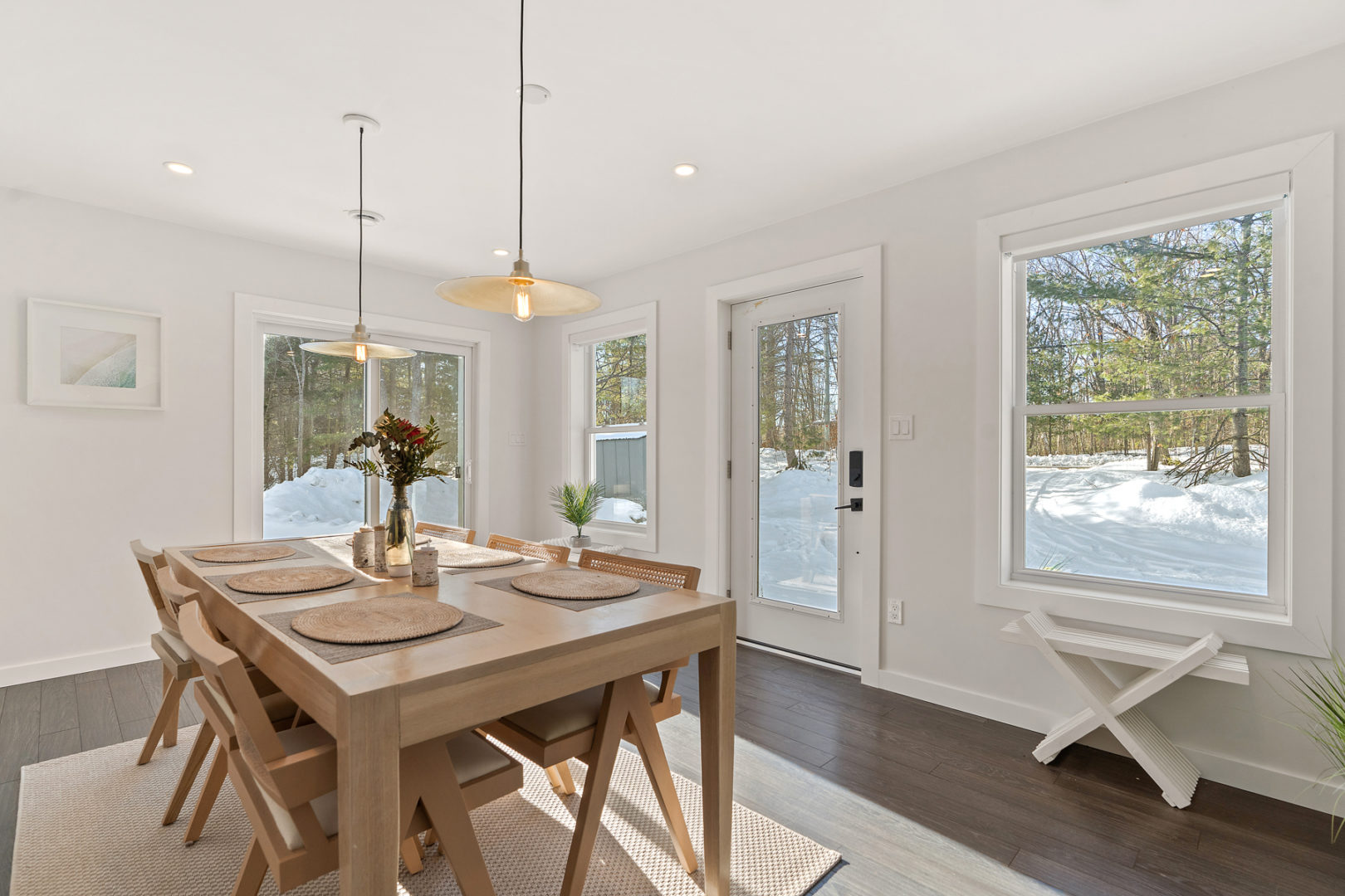 A bright sunroom dining area with plenty of windows and a walk-out door. A large wooden table and chairs sit in the middle of the room.