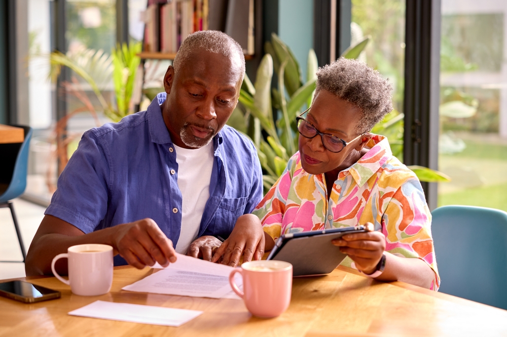 Senior Couple Sitting Around Table At Home Reviewing Finances Using Digital Tablet, considering renegotiating their mortgage