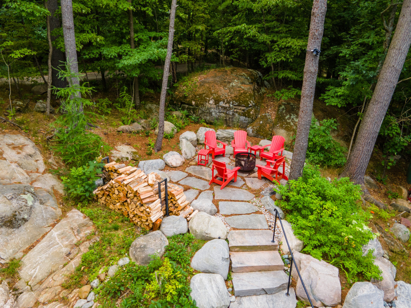 Stepping stones leading to a fire pit that is surrounded by red Muskoka chairs.