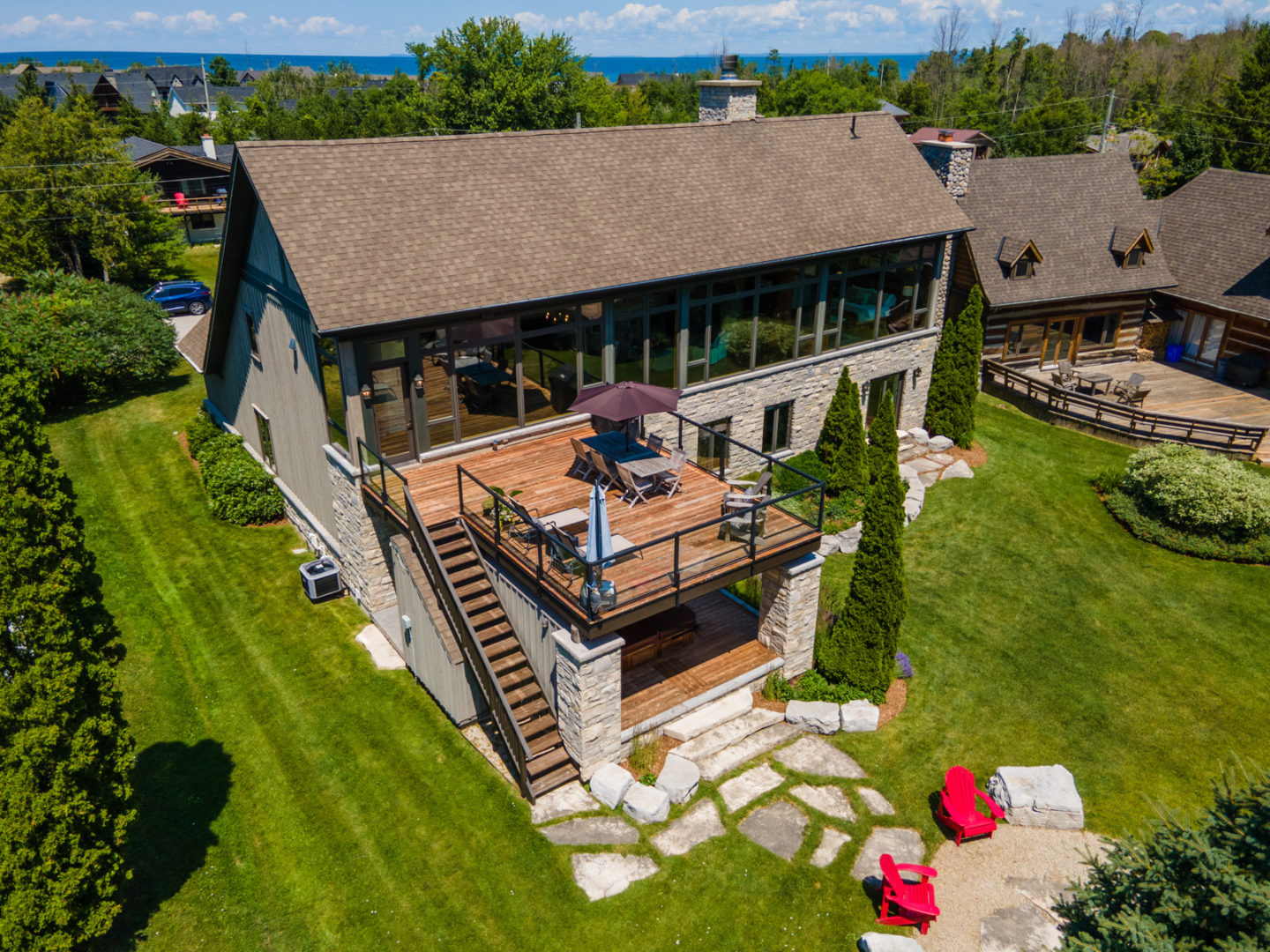 The back of a large two-story home with a big second-floor deck, a fire pit patio, and lots of windows.