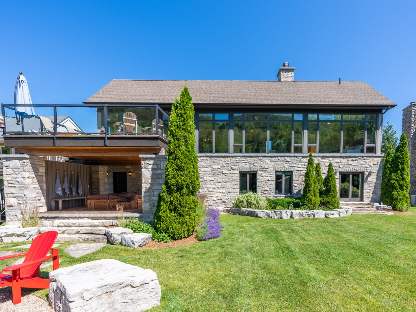 The back of a large, two-story home with green space, a second-floor deck, a fire pit, and a hot tub.