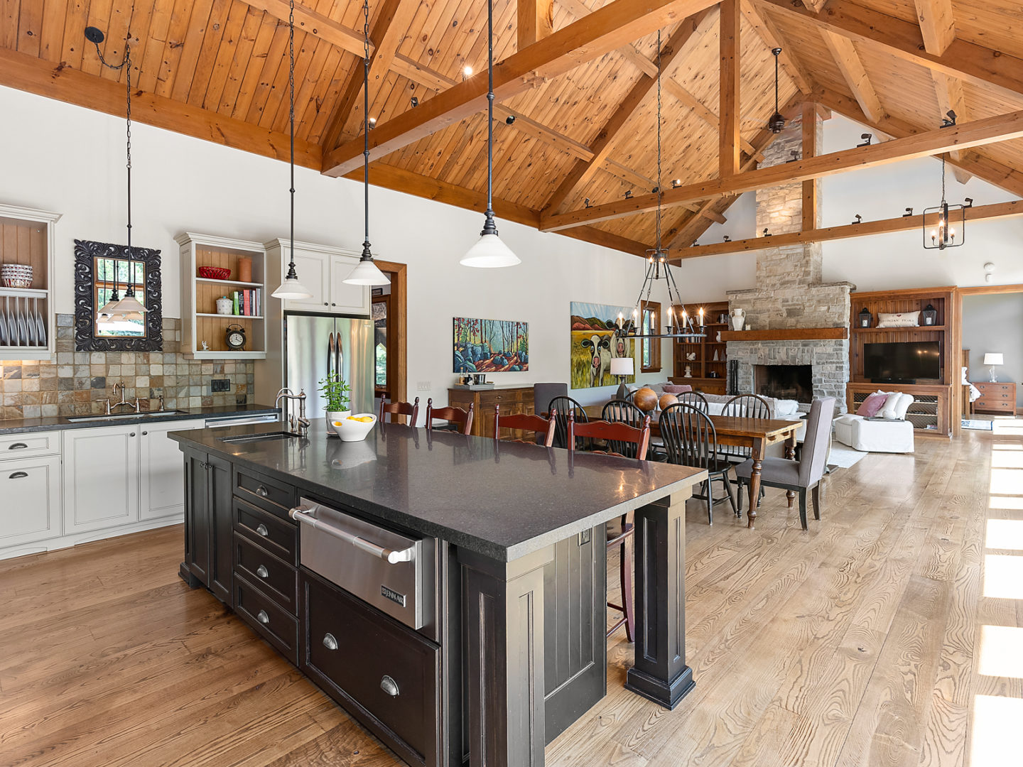 A large, open-concept living area with flow from the kitchen into the dining and living spaces. Wooden beams accent the high ceiling.