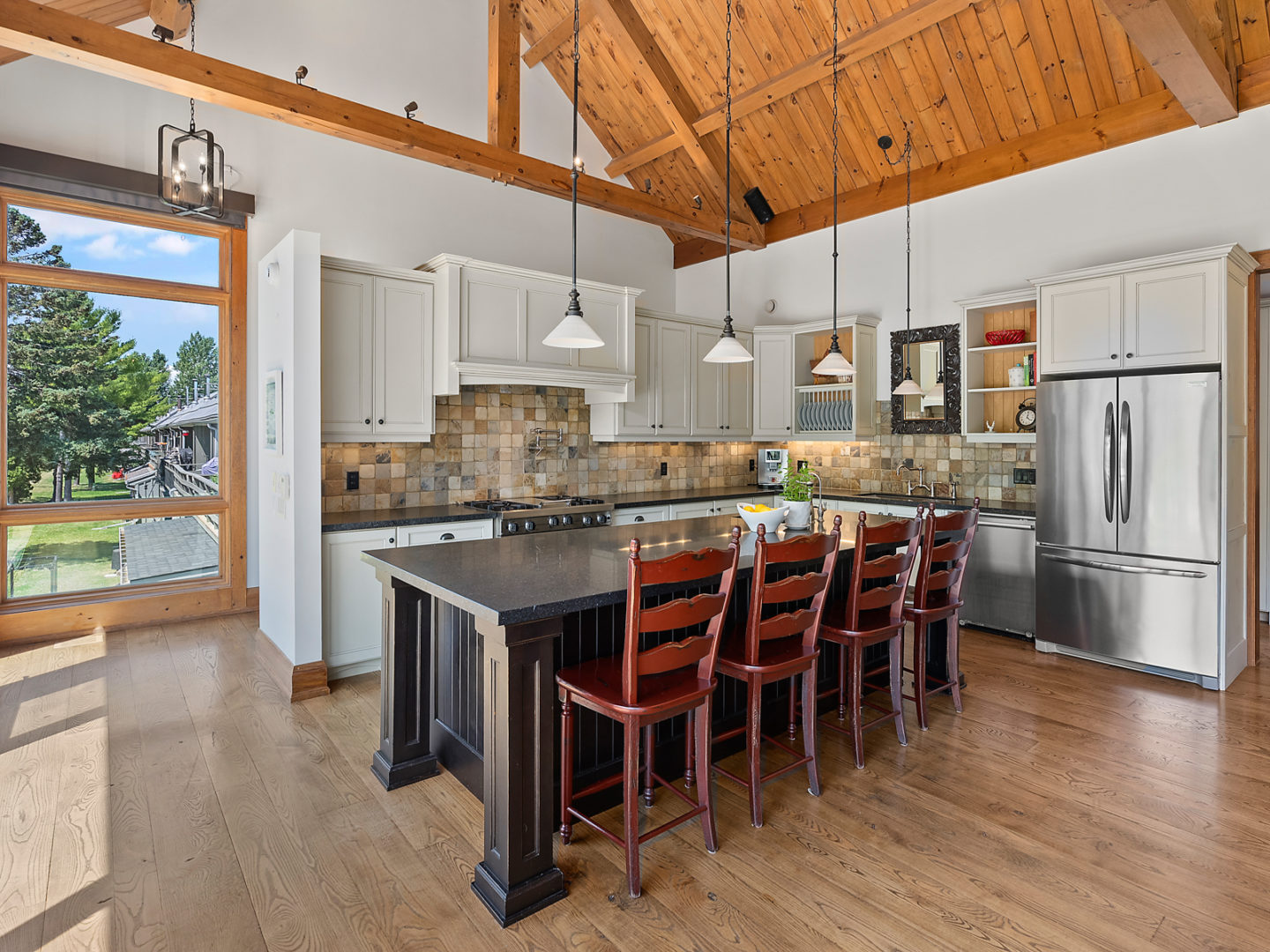 A large kitchen with a big island, modern appliances, and wooden beams accenting a high ceiling.