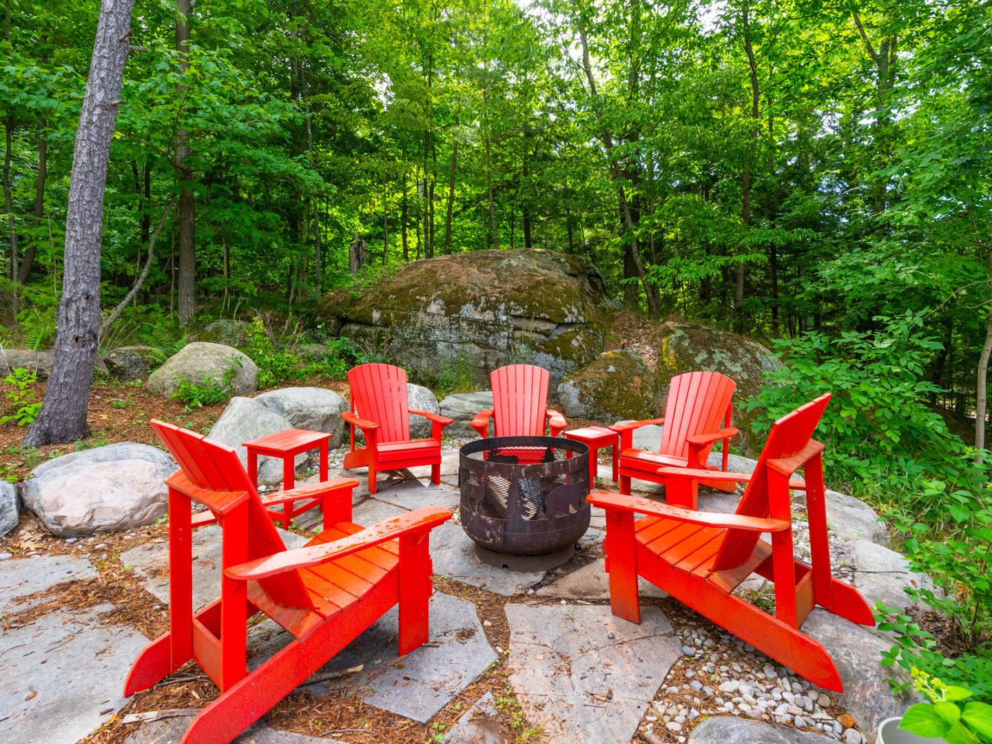 A fire pit area surrounded by red Muskoka chairs.