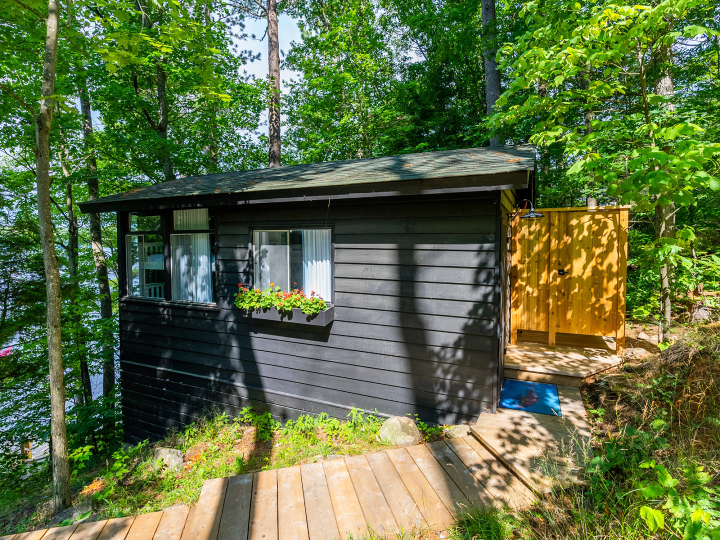 A wooden deck leads to a small bunkie with an outdoor shower off the side.