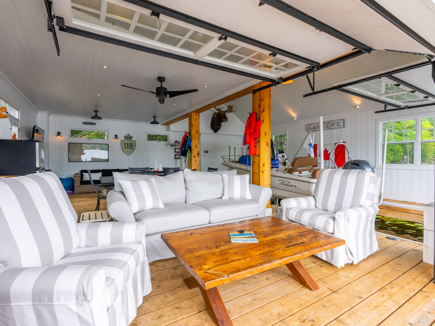 Interior of a boutique boathouse couches, a dining area, and a boat parked to the side.