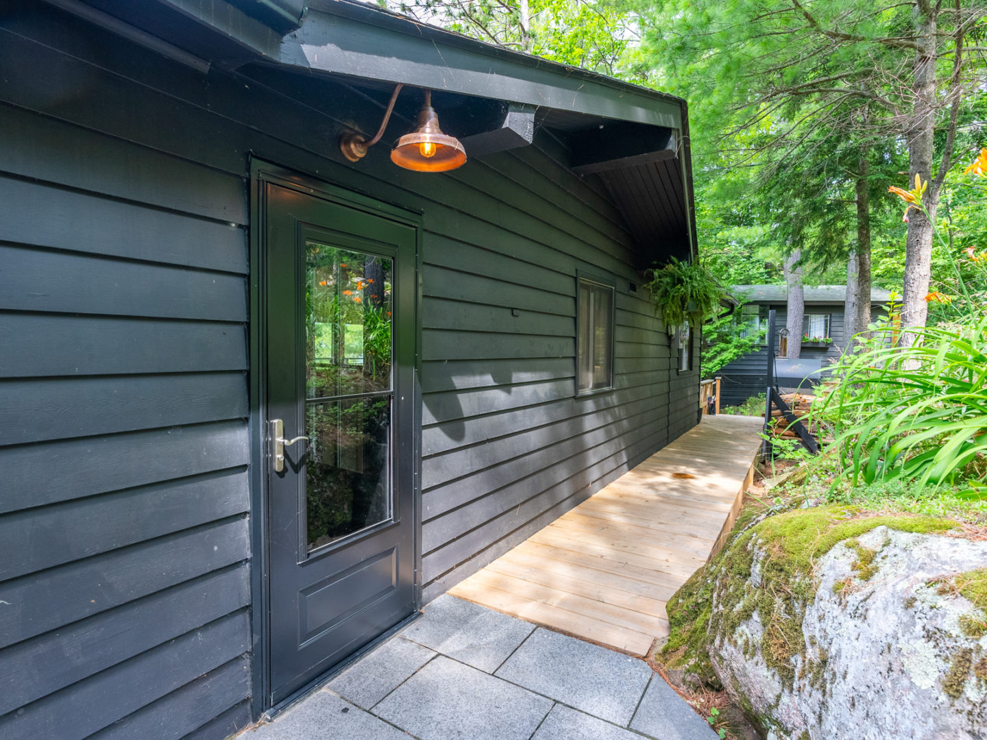 The front door of a cottage with a wrap-around deck and a dark grey exterior.