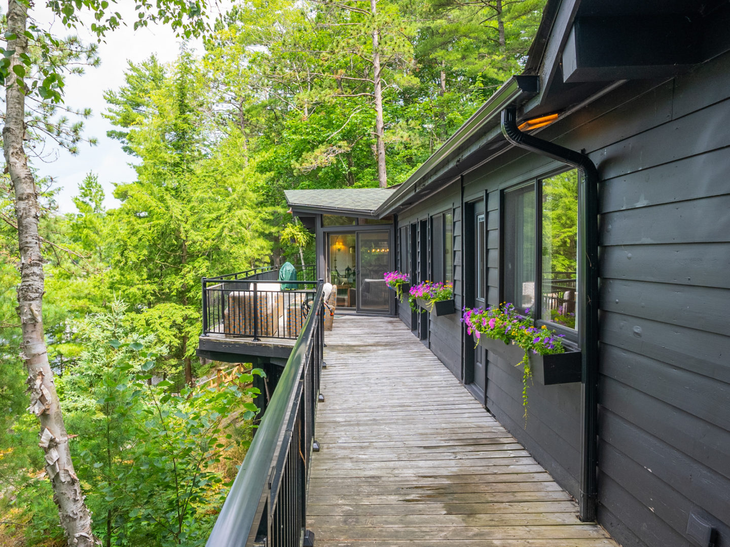 A wrap-around deck on the side of a large cottage, surrounded by trees and greenery.