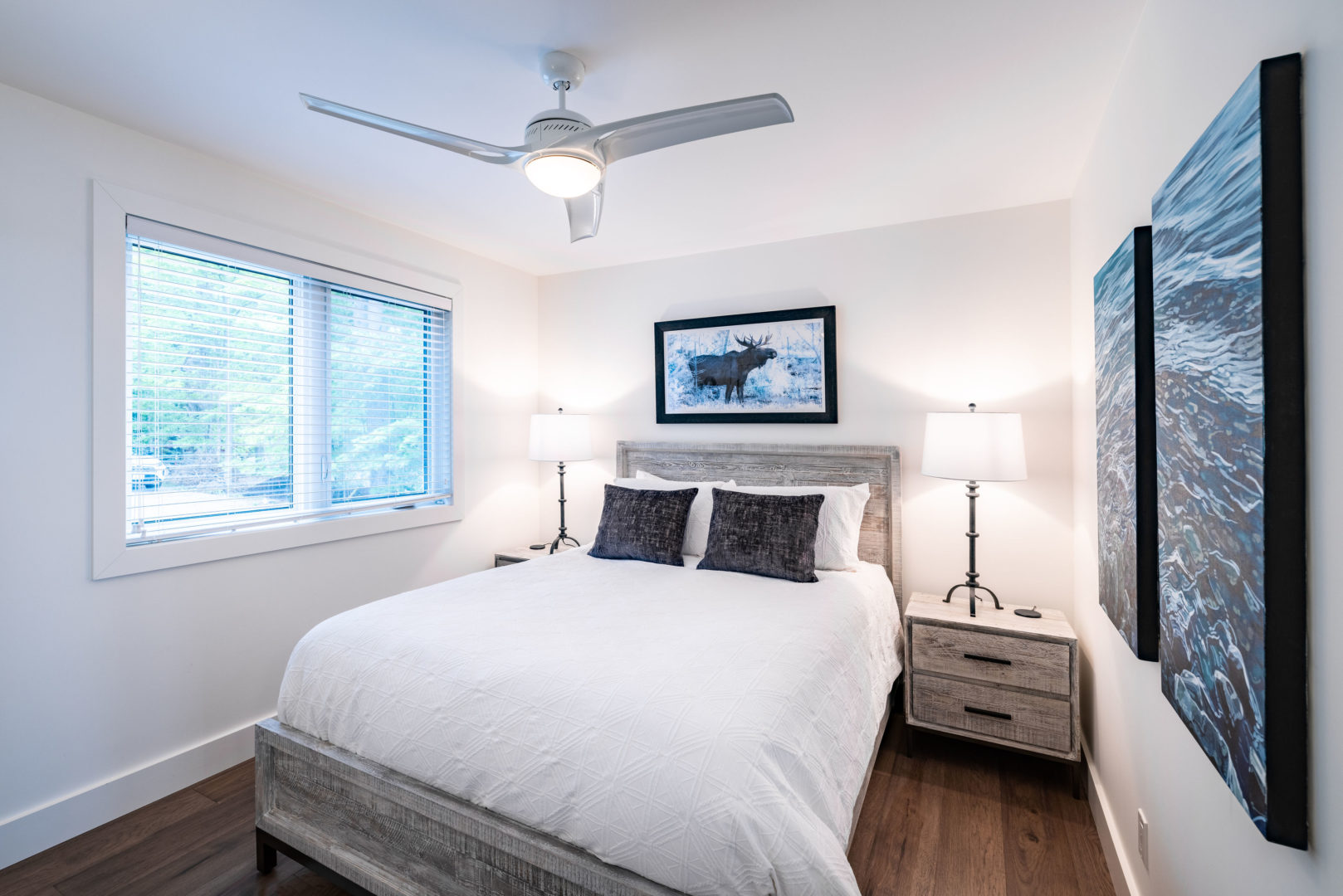 A bright, simple bedroom with a bed, a ceiling fan, and a big window.