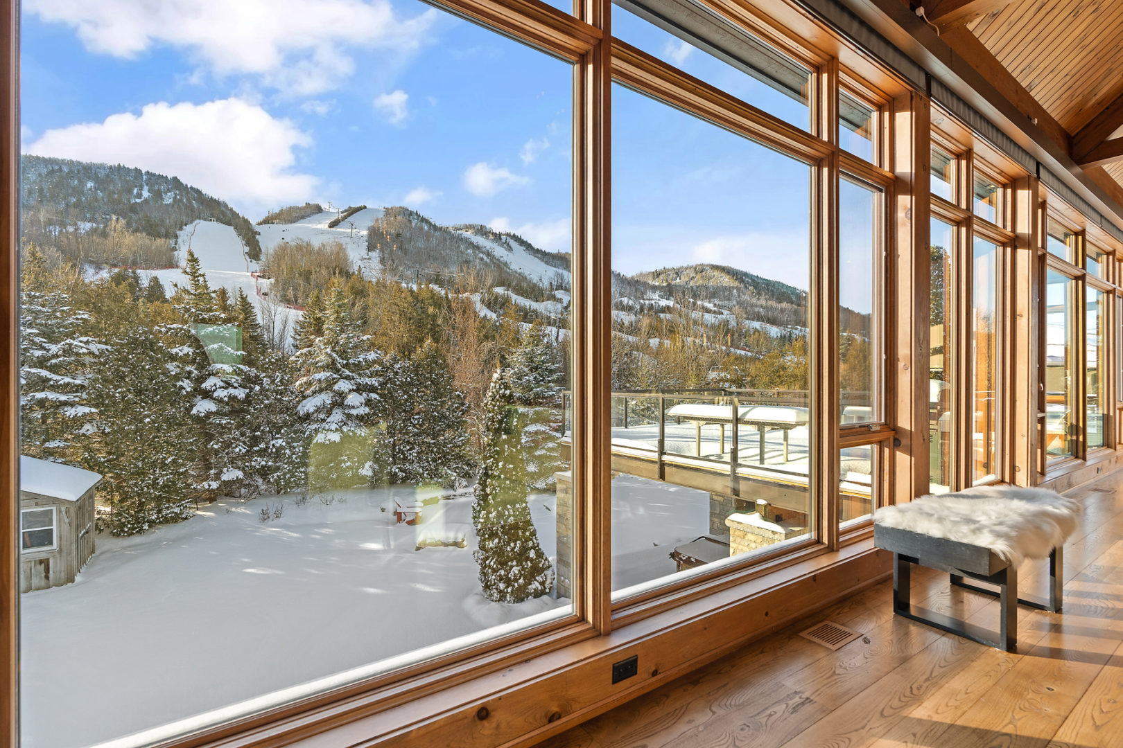 Large windows stretching along the side of a house. The view looks out on a sloping mountain covered in snowy trees.