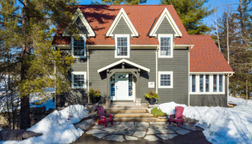 The front of a large lakefront home with a greenish grey exterior and a red roof.