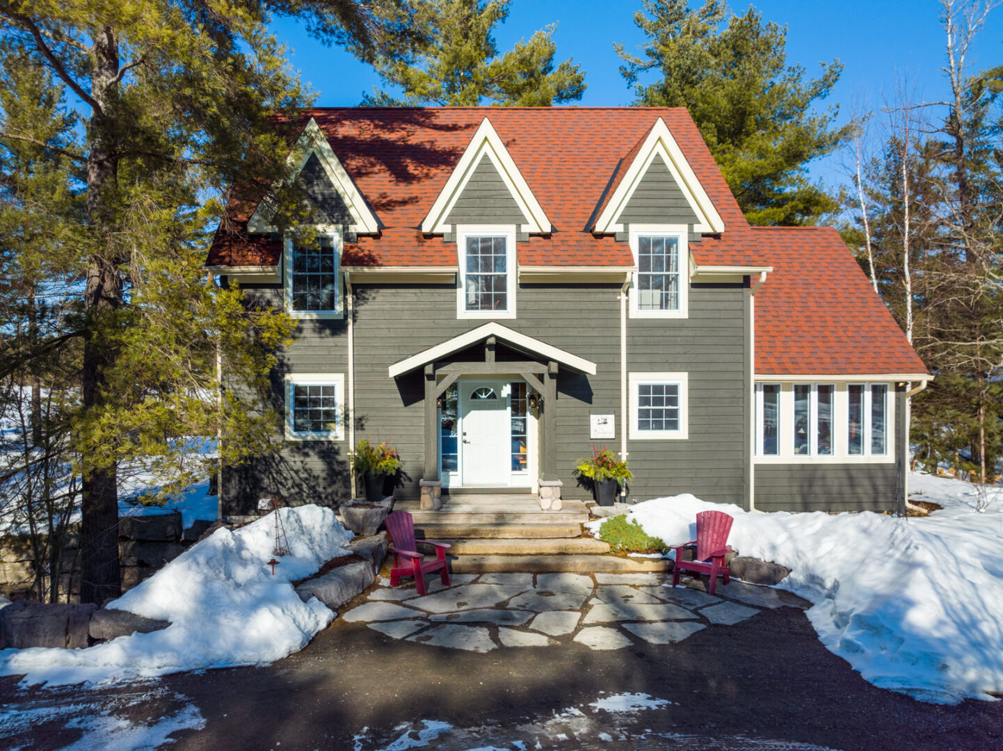 The front of a large lakefront home with a greenish grey exterior and a red roof.