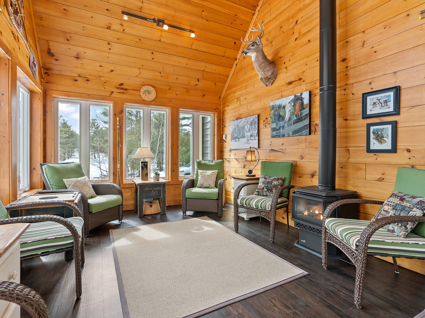 A sunny sitting room with ample seating, plenty of windows, and vaulted ceilings. Warm wood-panelled walls and ceilings and a wood-burning fireplace complete the space.