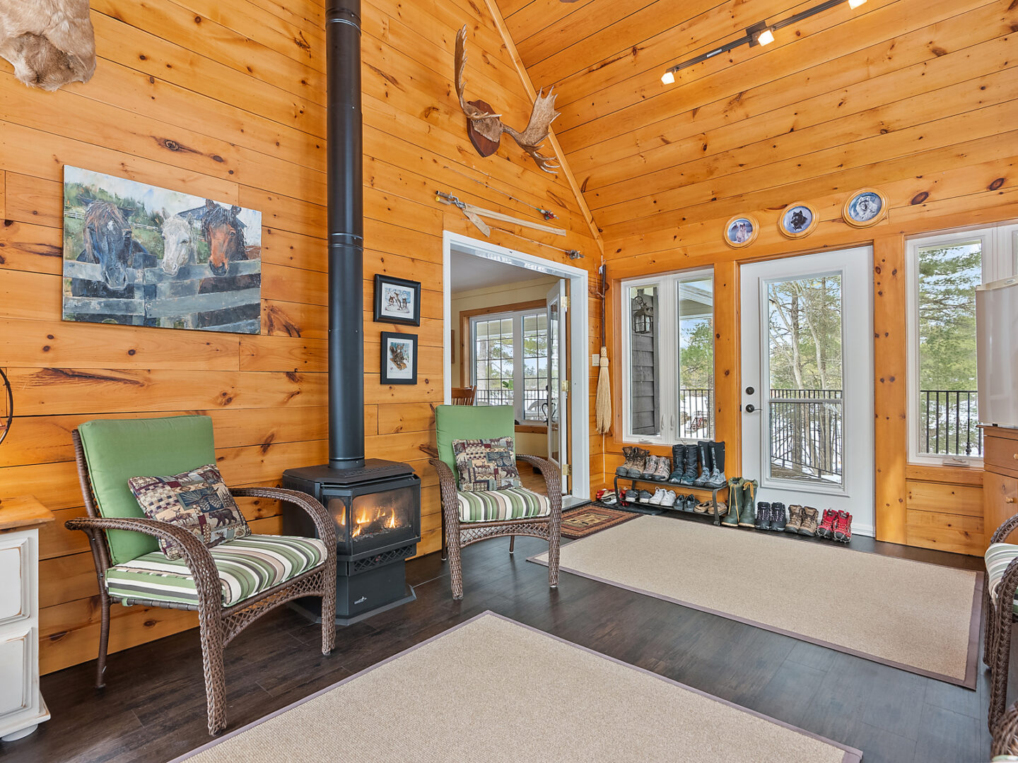 A sunny sitting room with ample seating, plenty of windows, and vaulted ceilings. Warm wood-panelled walls and ceilings and a wood-burning fireplace complete the space.