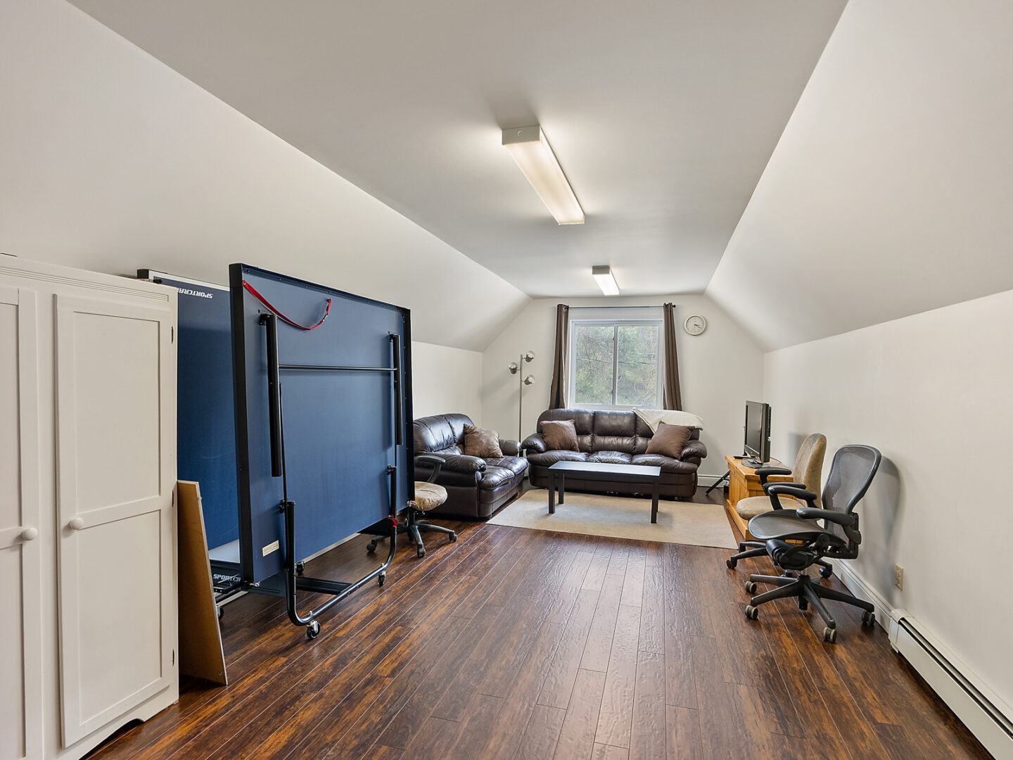 A narrow loft space above a garage, with hardwood floors and a seating area.
