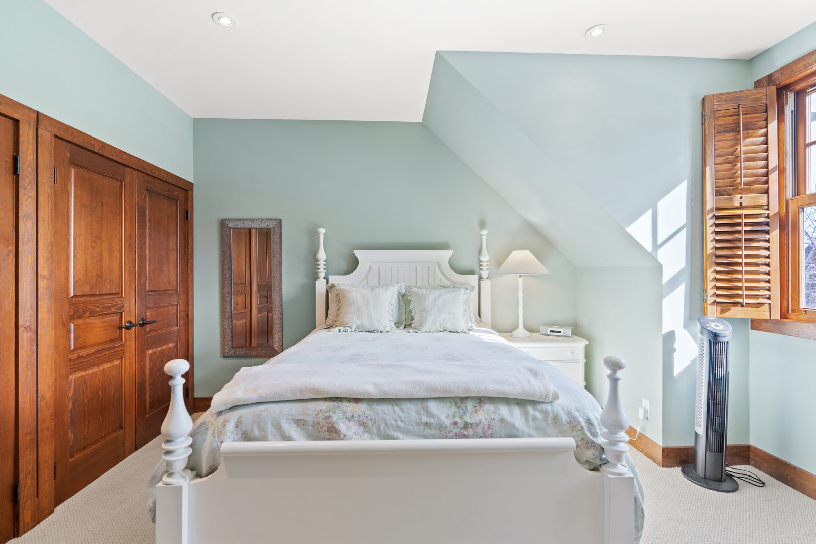 A bright bedroom with seafoam-coloured walls and a large bed.