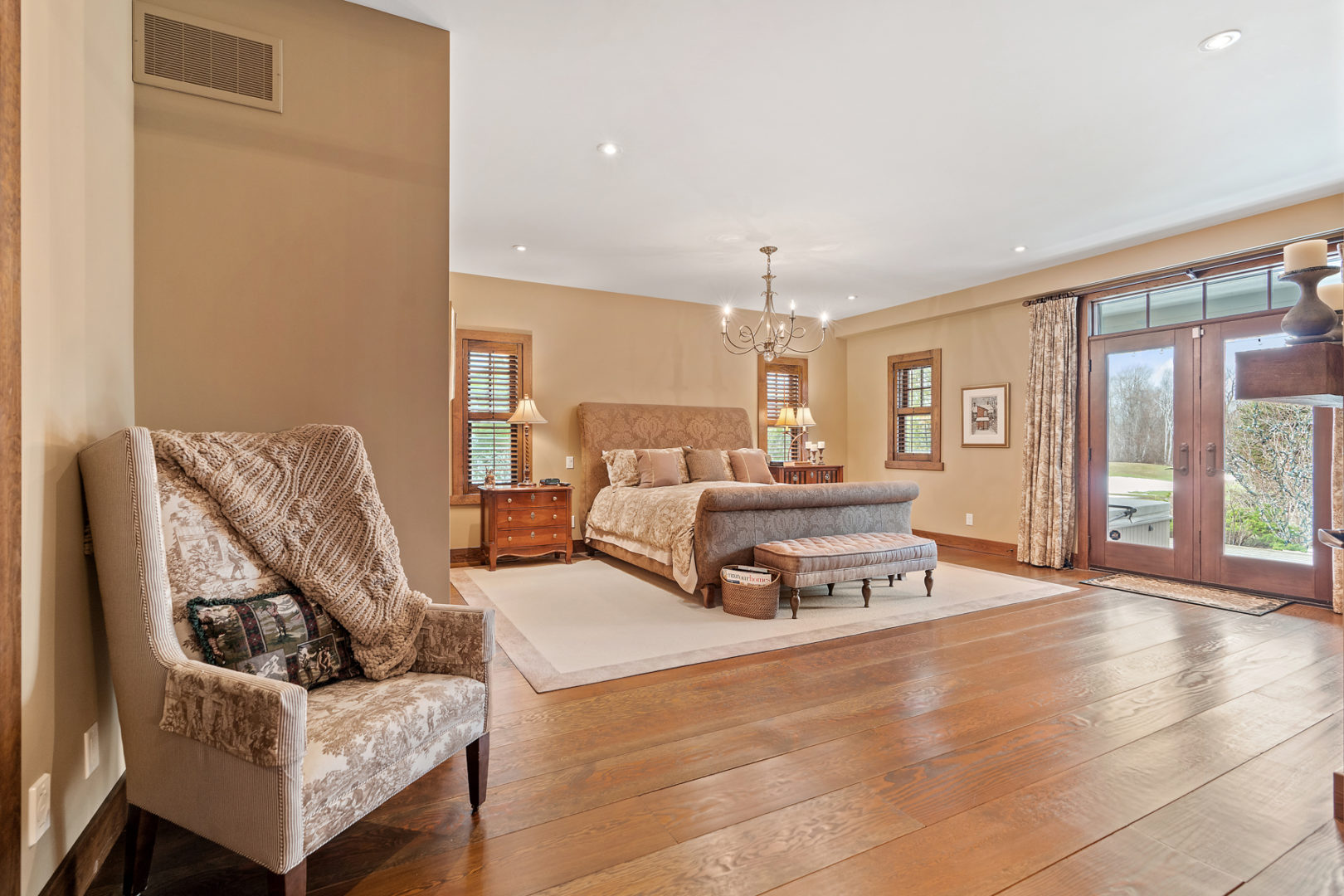 A huge primary bedroom with tons of floor space, a large bed, and double doors leading out to a backyard area with a hot tub.