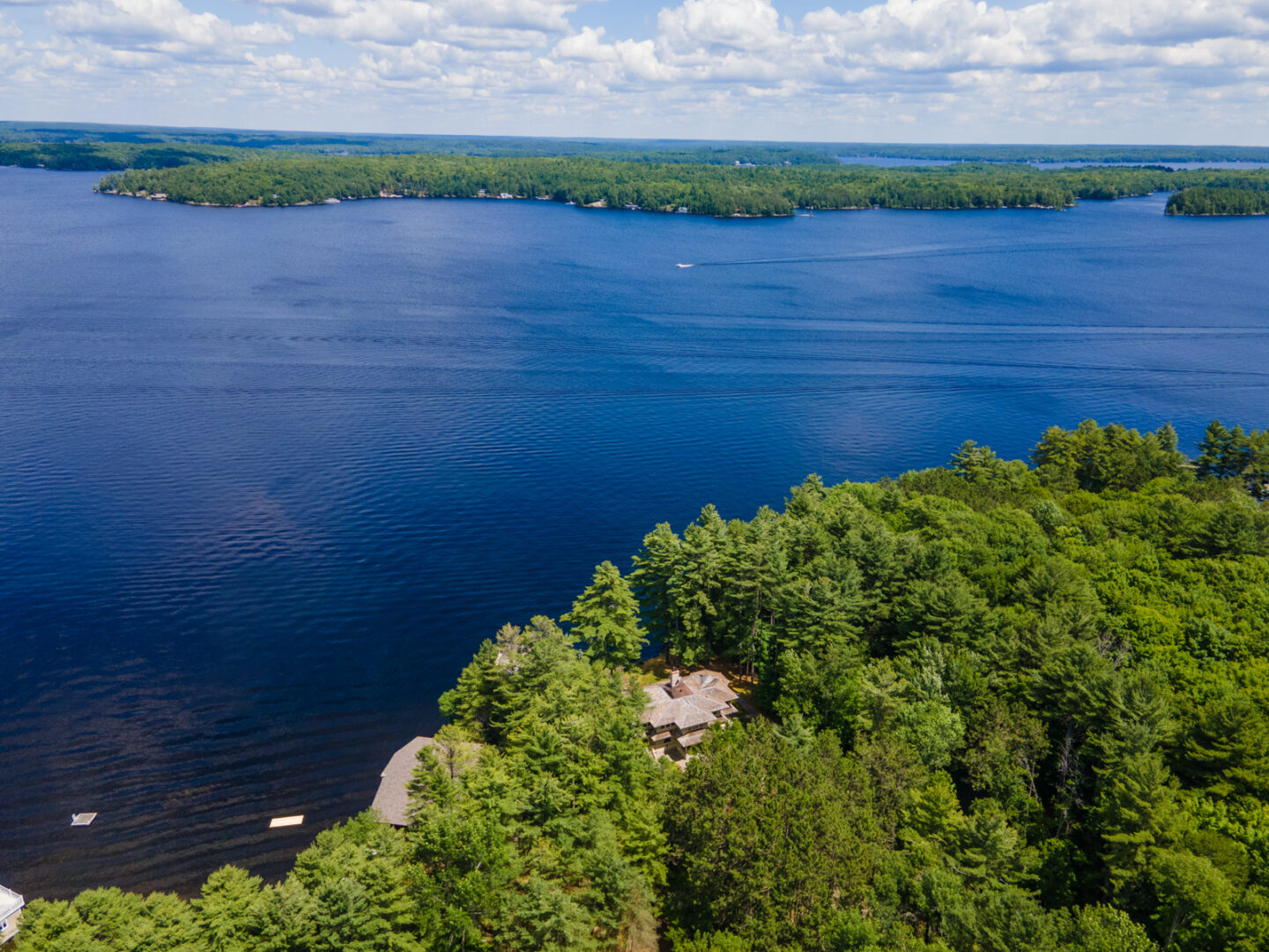 A shoreline with green trees and a large cottage, looking out to a blue lake.
