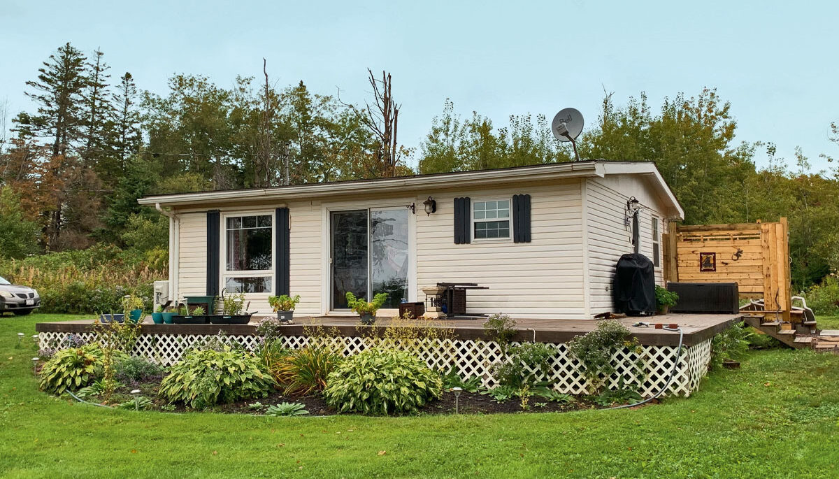 A cottage in PEI with white siding and a large deck, surrounded by a green lawn and trees