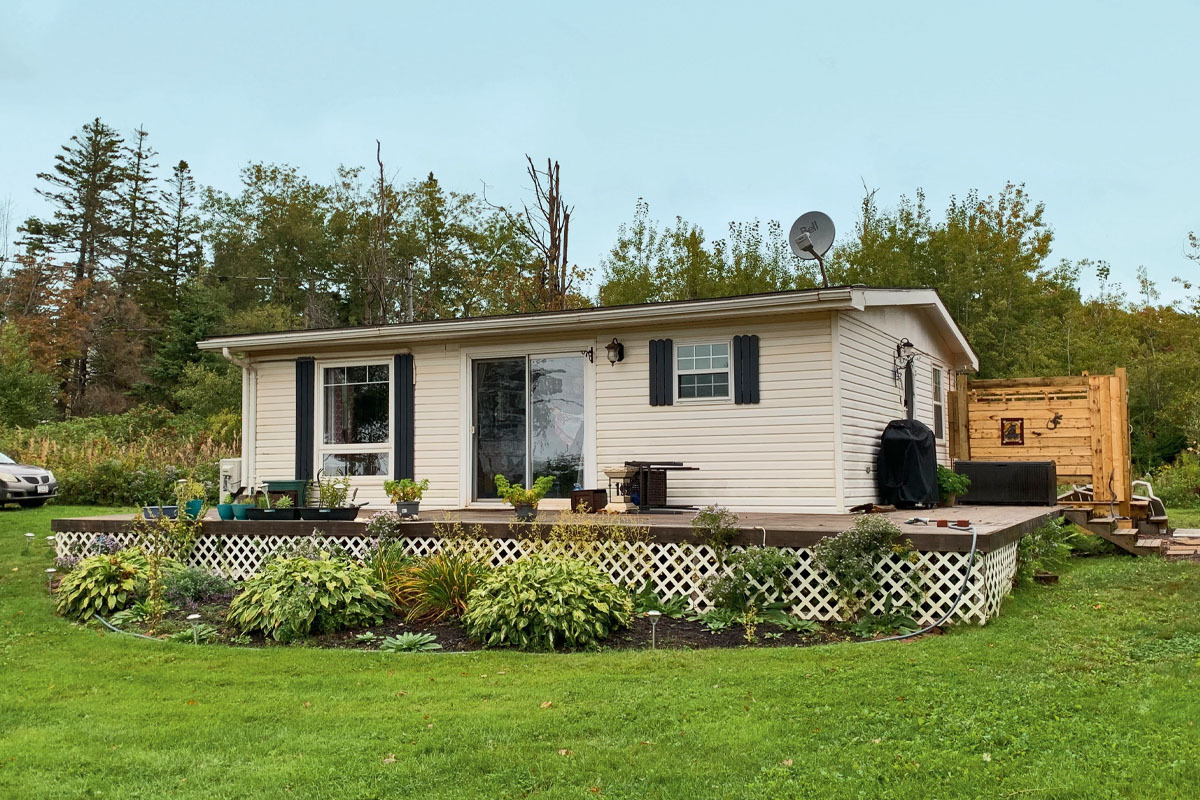 A cottage in PEI with white siding and a large deck, surrounded by a green lawn and trees