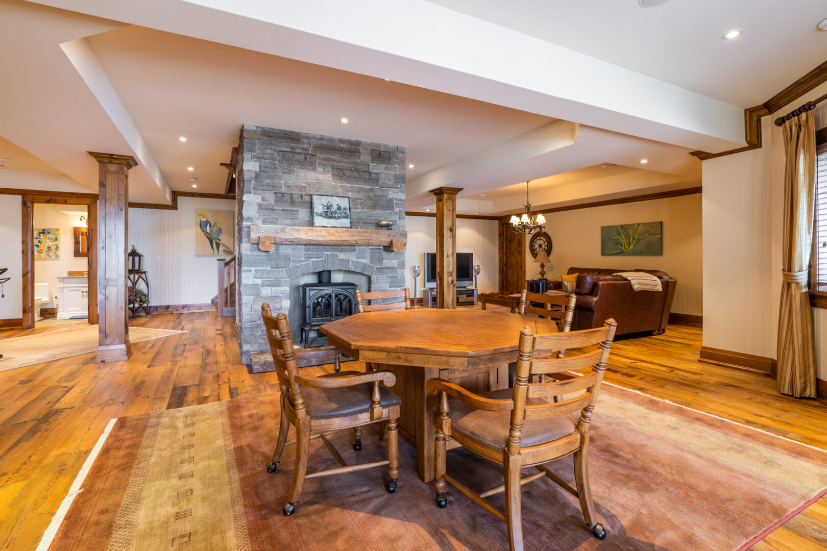 A spacious lower-level living area with a dining table and chairs in the middle of the room, a central stone fireplace, and a living area with couches.