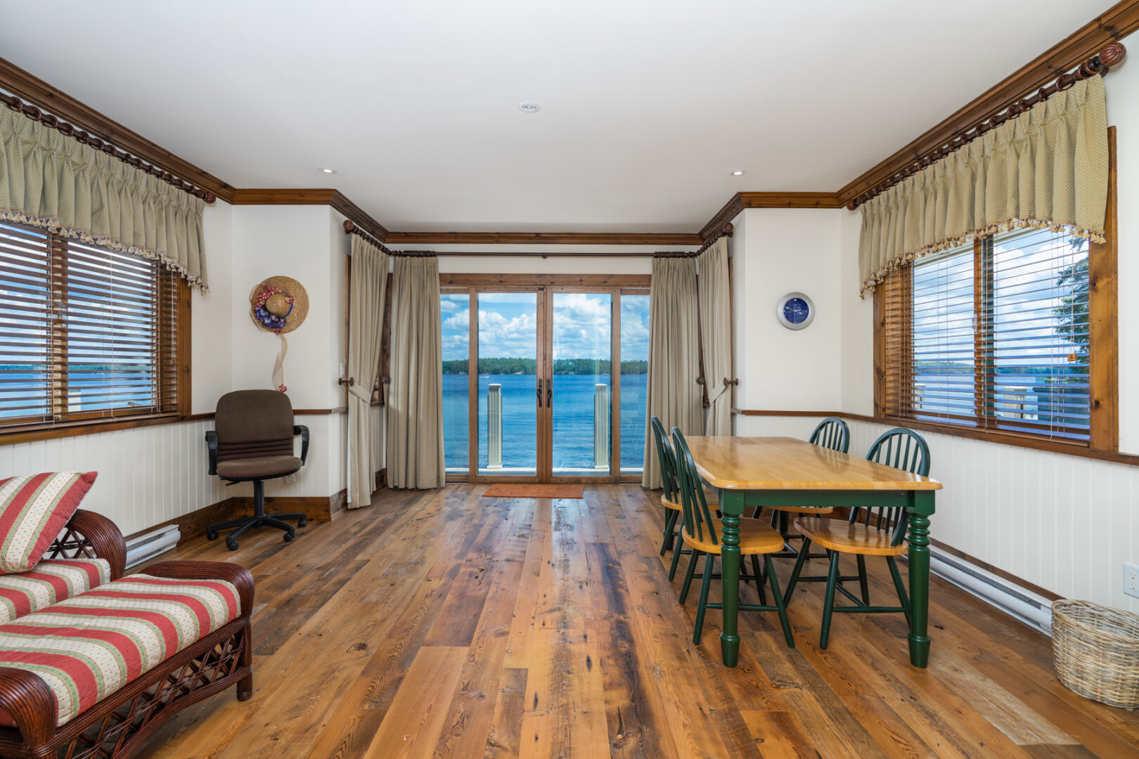 A spacious boathouse living space with large windows overlooking the lake, a small dining table, and chairs.