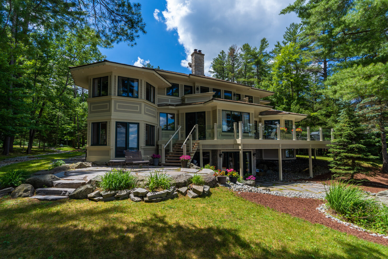 The back of a large, luxury cottage with lots of windows, a landscaped patio and garden area, and a large balcony.