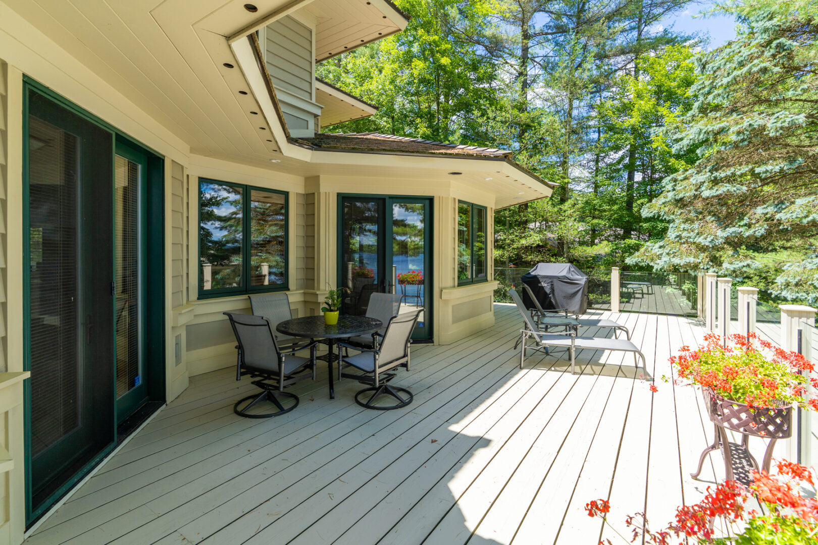 A large balcony deck extending off a cottage with lots of windows, with a seating area and a barbecue.