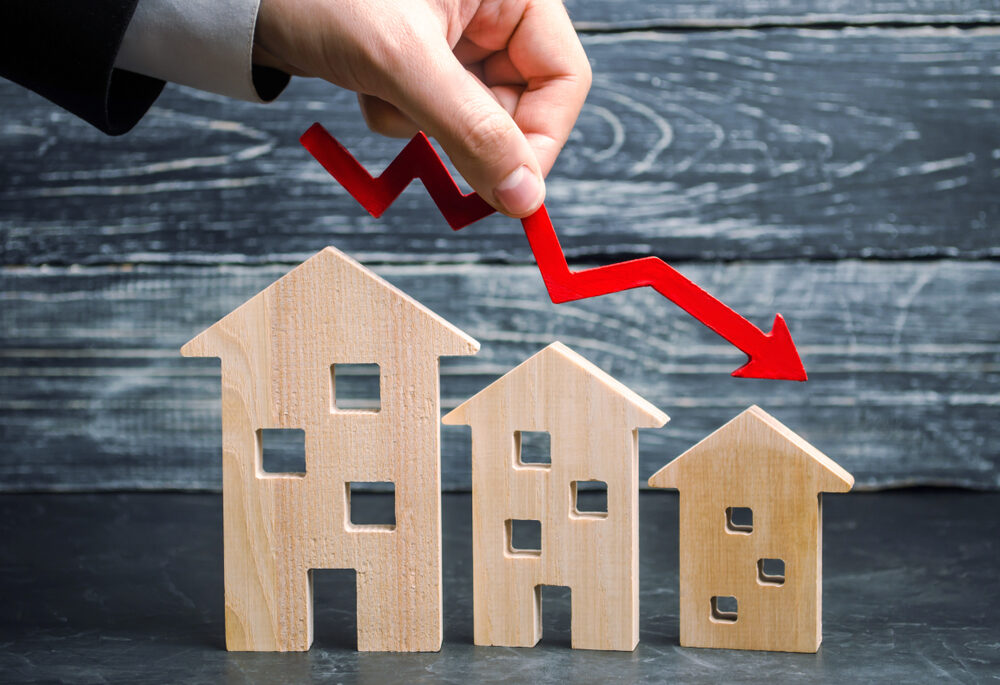 a decline in property prices shown as a red arrow going down above three wooden houses