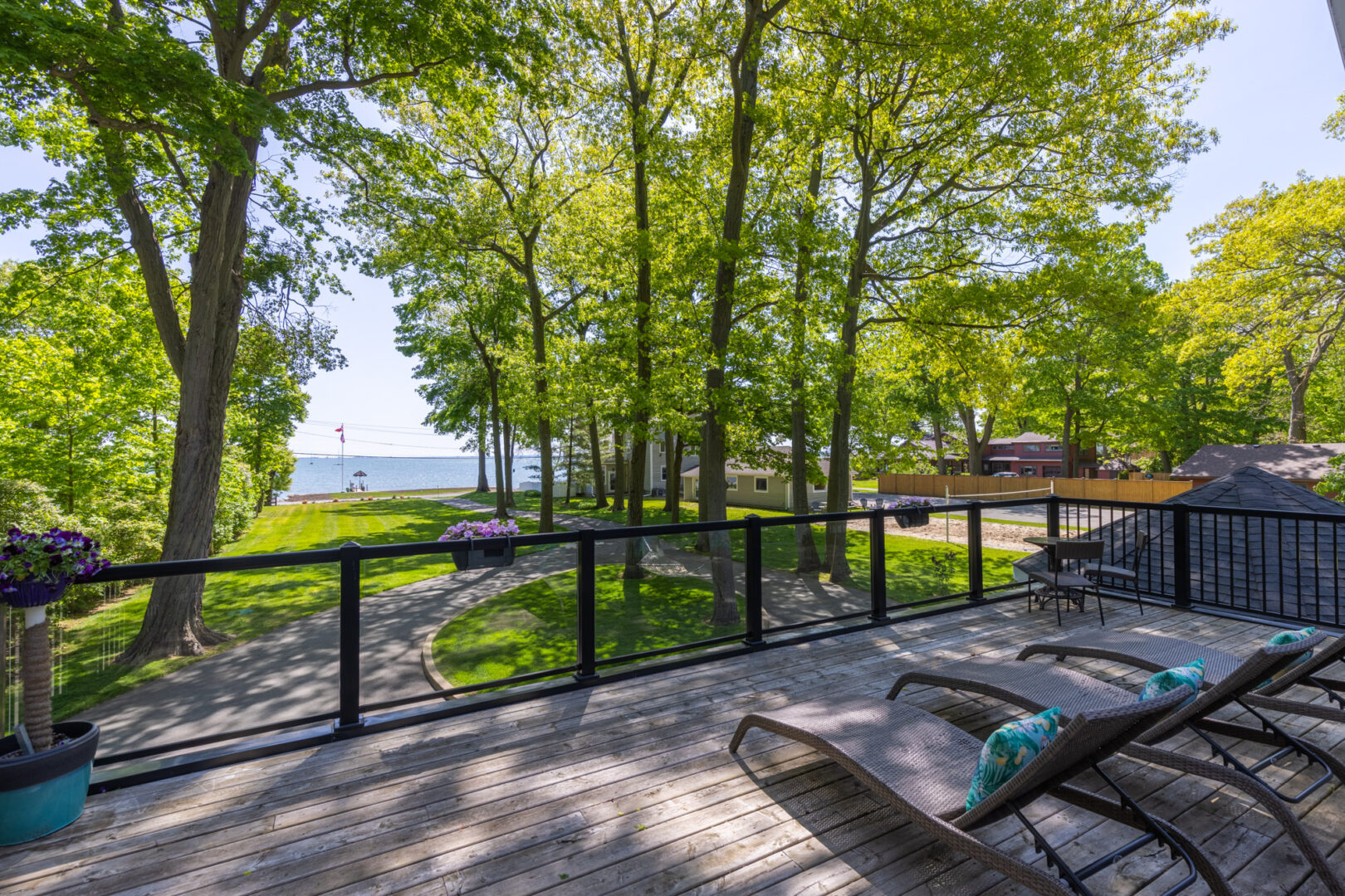 A large balcony with a glass railing and two lounger chairs, looking out over a large grassy property and a lake.