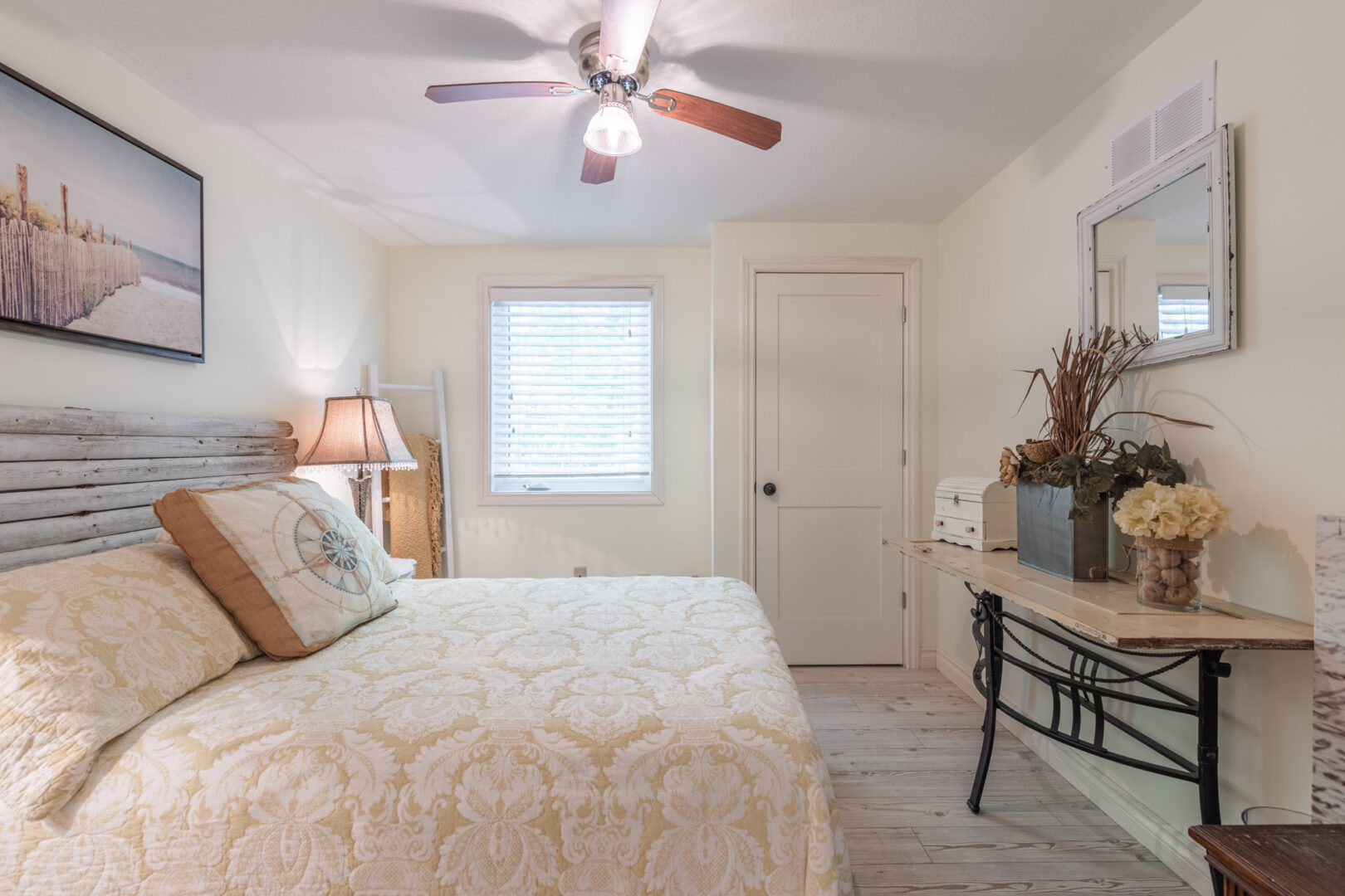 A small, bright bedroom with a big bed, a small window, and a ceiling fan.