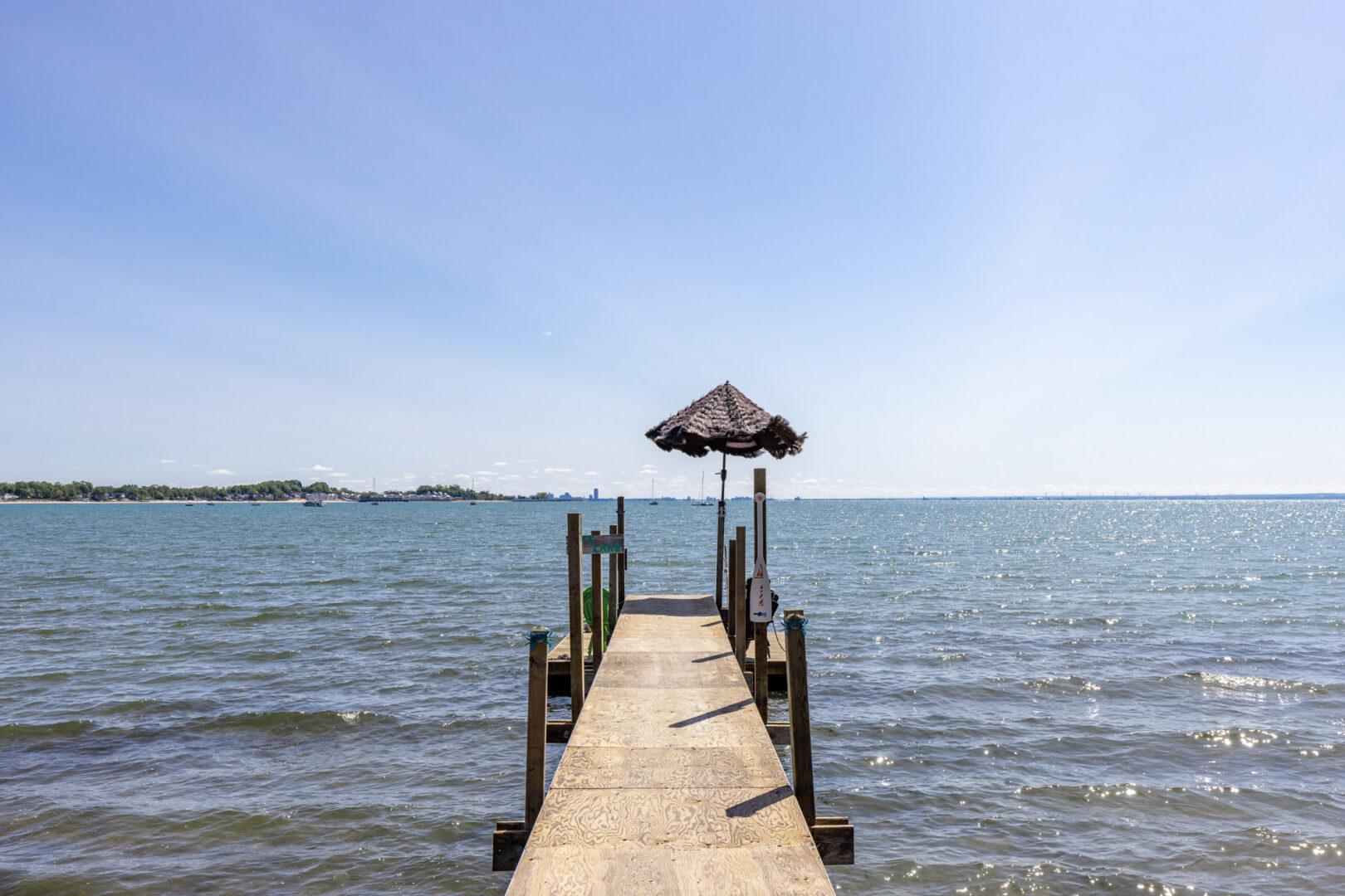 A long, narrow dock with an umbrella on the end stretches into a blue lake.