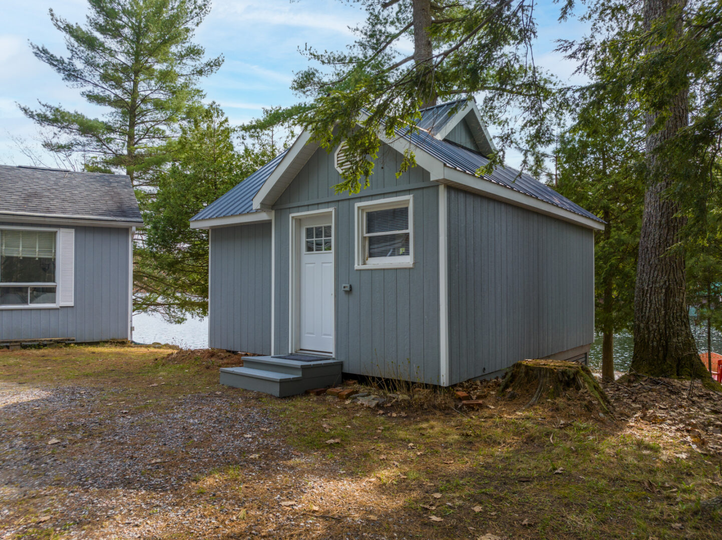 Exterior of a small bunkie that sits beside a cottage, surrounded by trees.