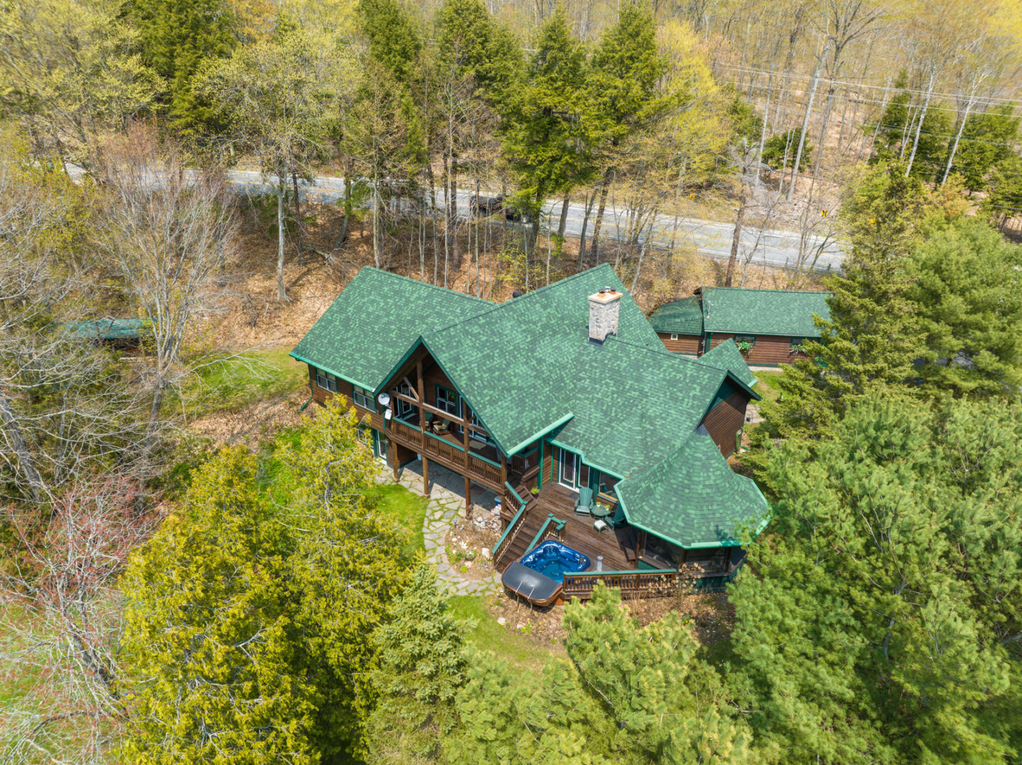 A large cottage with a green roof sits just off the road, surrounded by trees.
