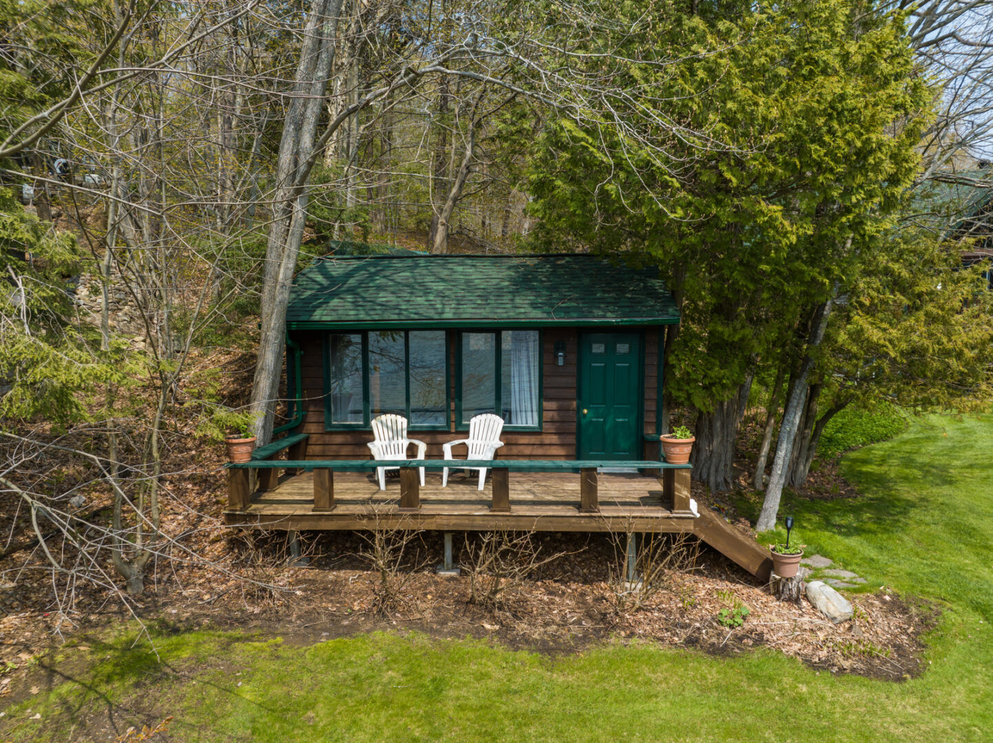 A small guest bunkie with a green roof and a little deck with two chairs.