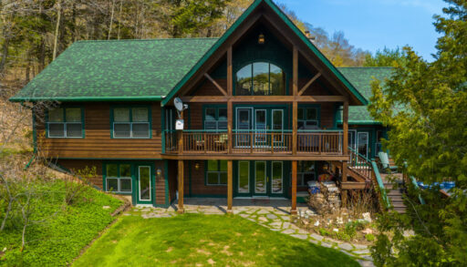 Water-facing exterior of a large cottage that has a green roof, dark wood exterior, and lots of deck space extending off two levels.