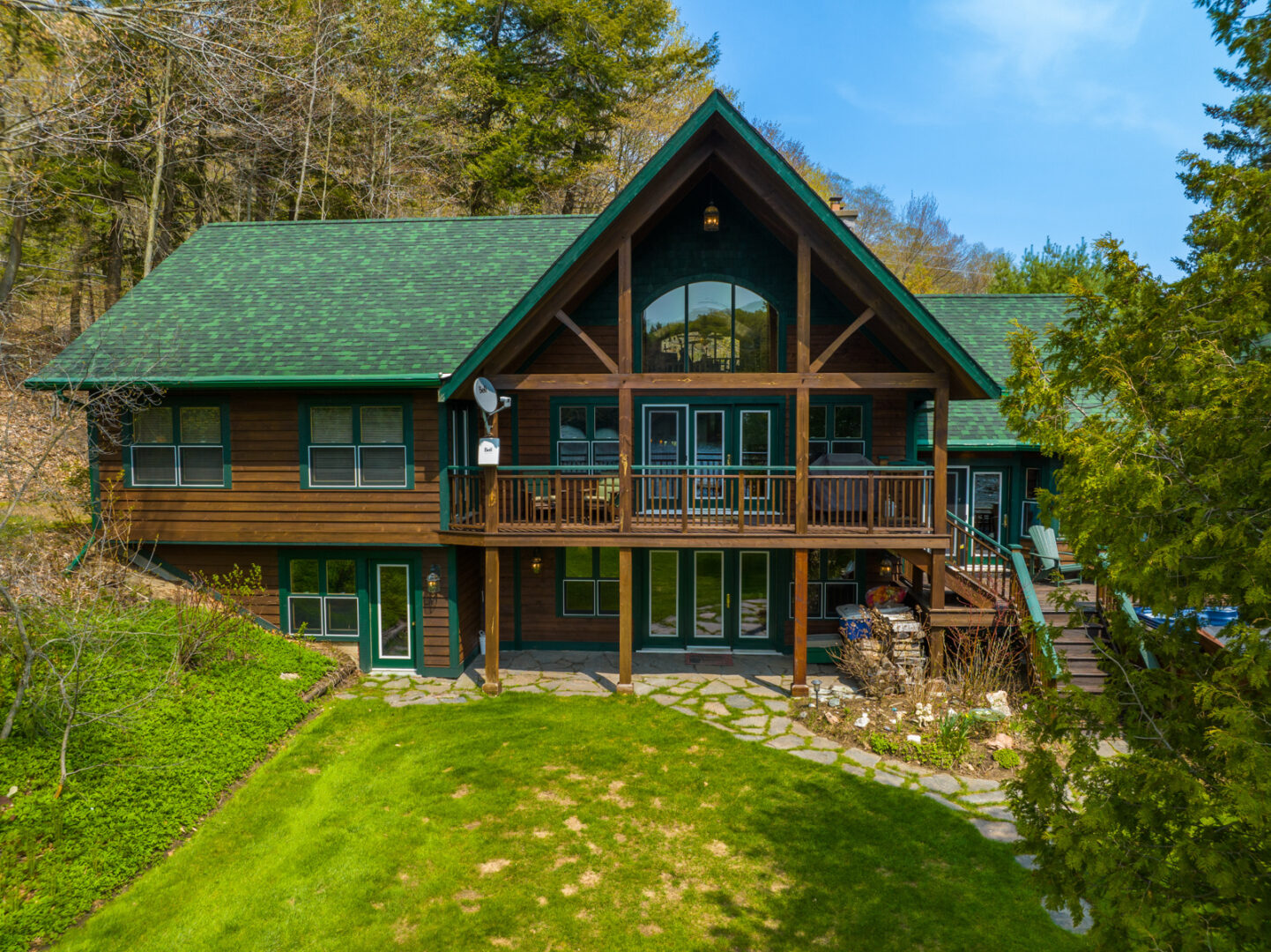 Water-facing exterior of a large cottage that has a green roof, dark wood exterior, and lots of deck space extending off two levels.